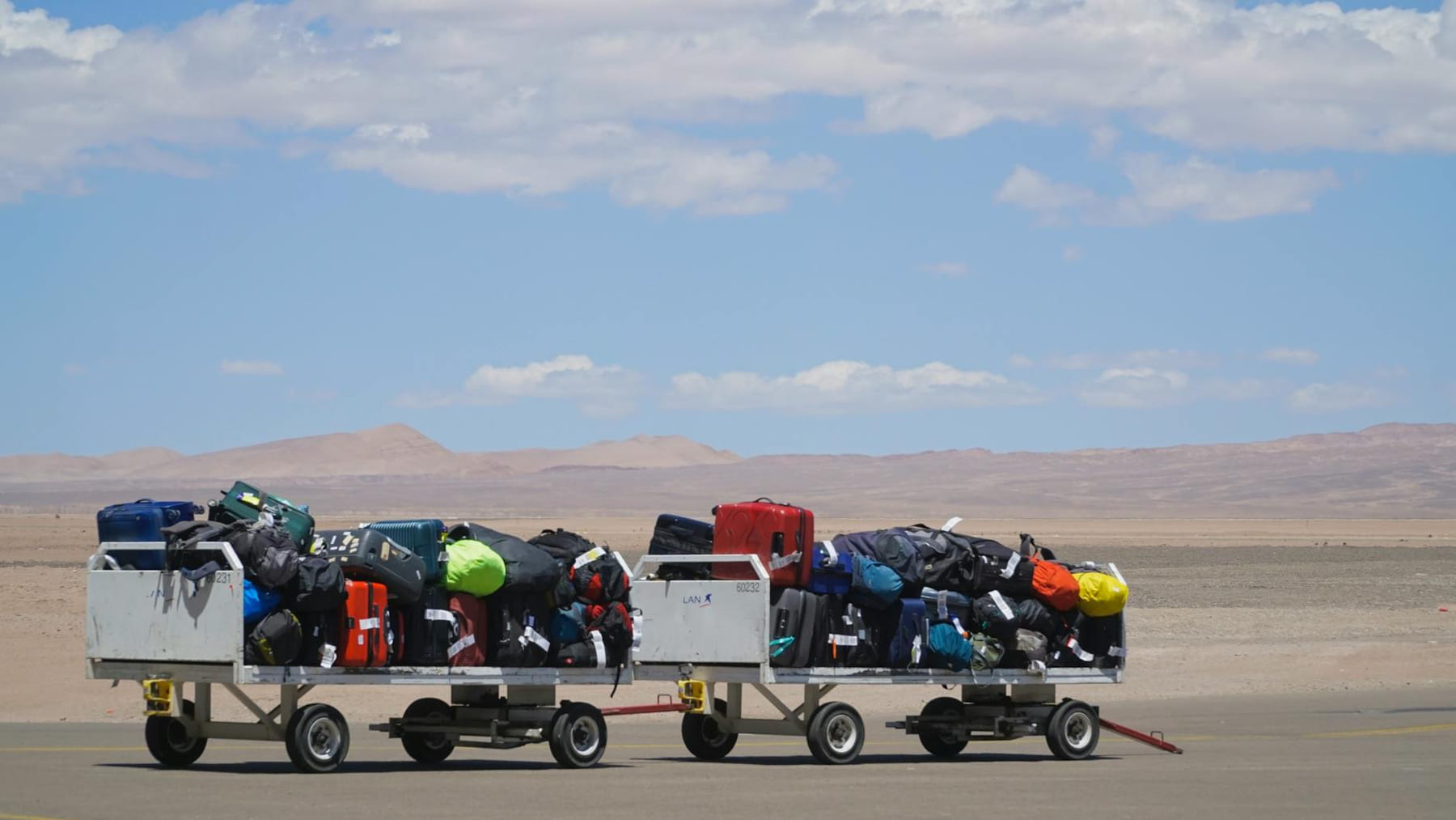 Luggage carts at airport loaded with colorful bags under clear sky. Outdoor travel scene. on Miles and Memories