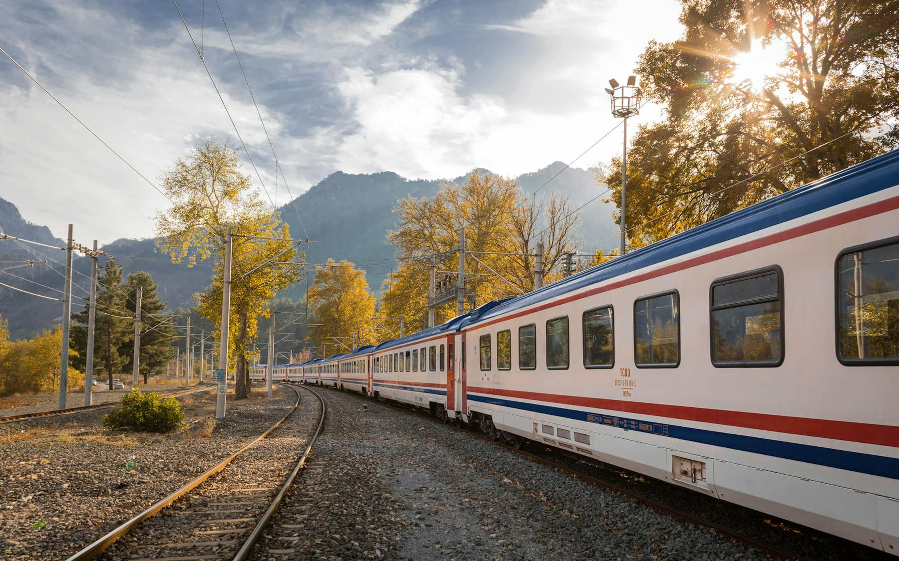 A picturesque train travels through a vibrant autumn landscape with mountains. on Miles and Memories