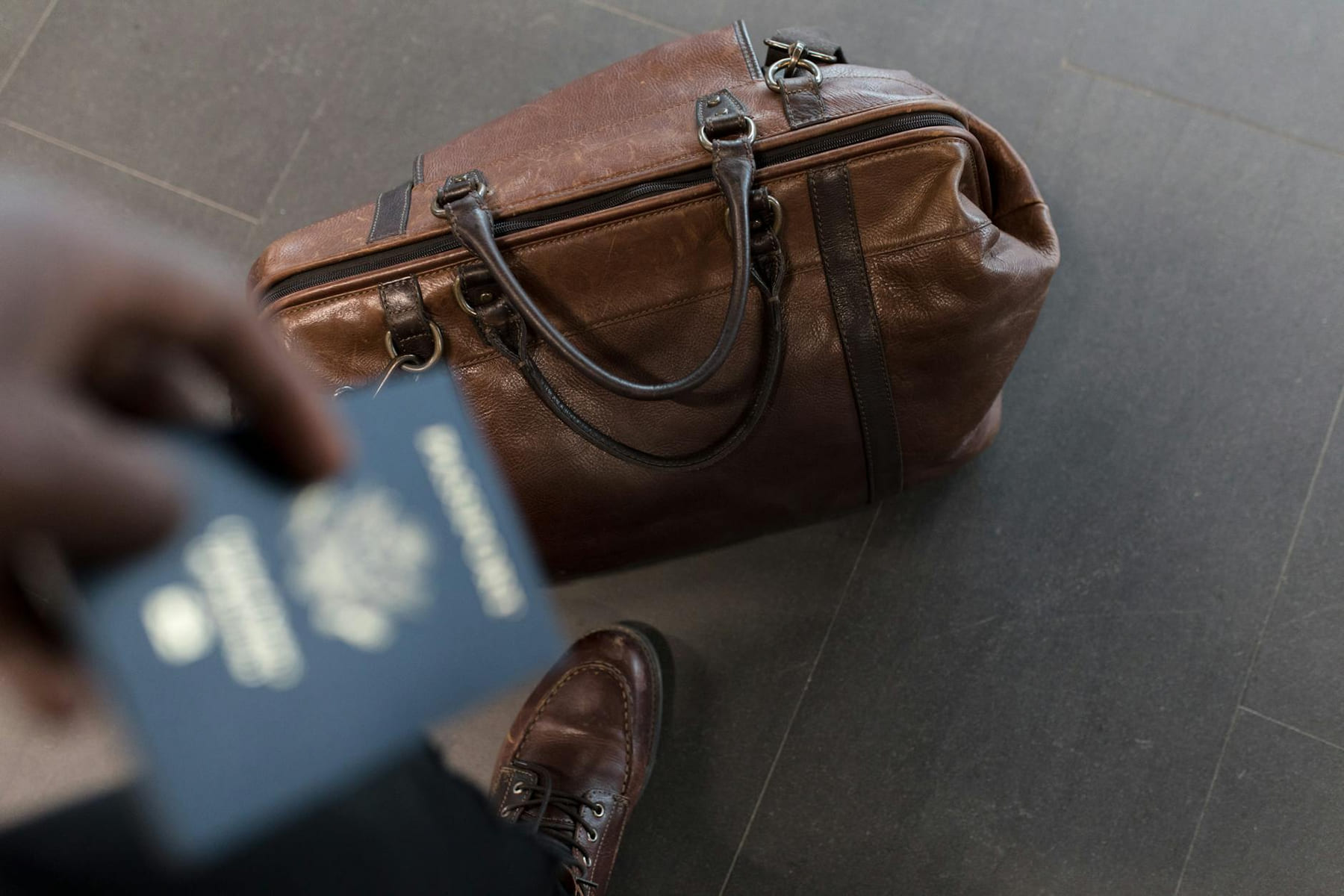 Brown leather bag with passport in an airport setting, ideal for travel and fashion themes. on Miles and Memories