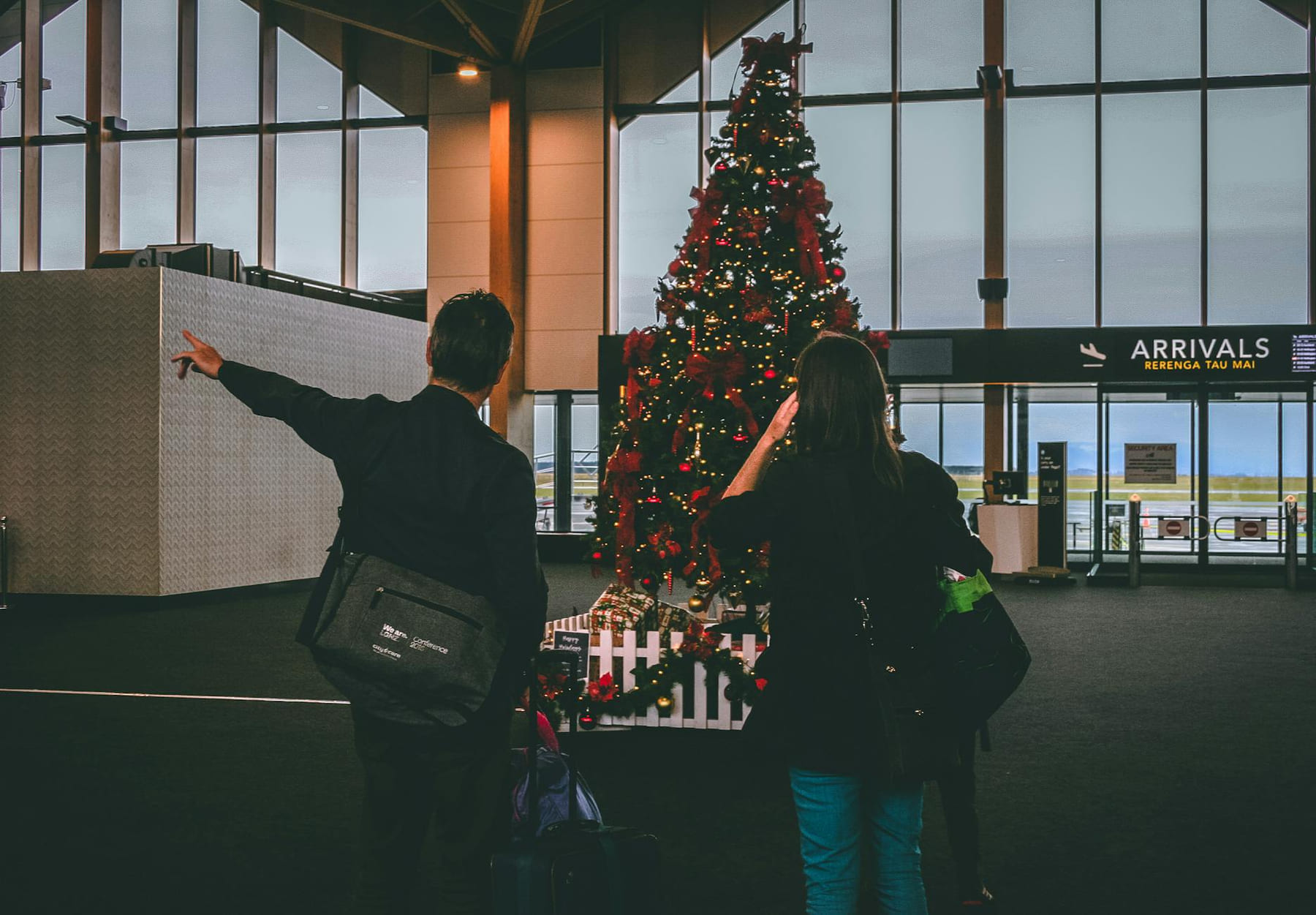 Young couple observes Christmas tree inside airport terminal. on Miles and Memories