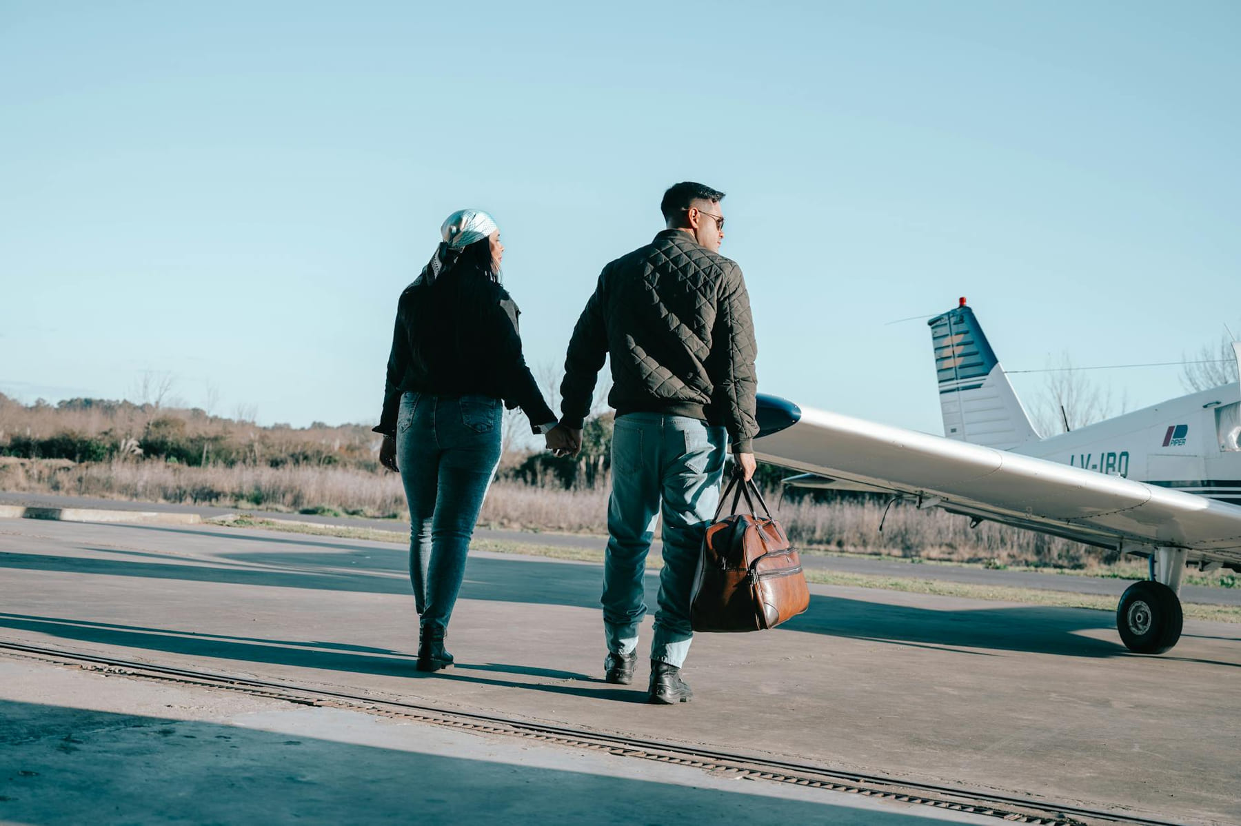 Man and woman holding hands near private plane on a clear autumn day. on Miles and Memories