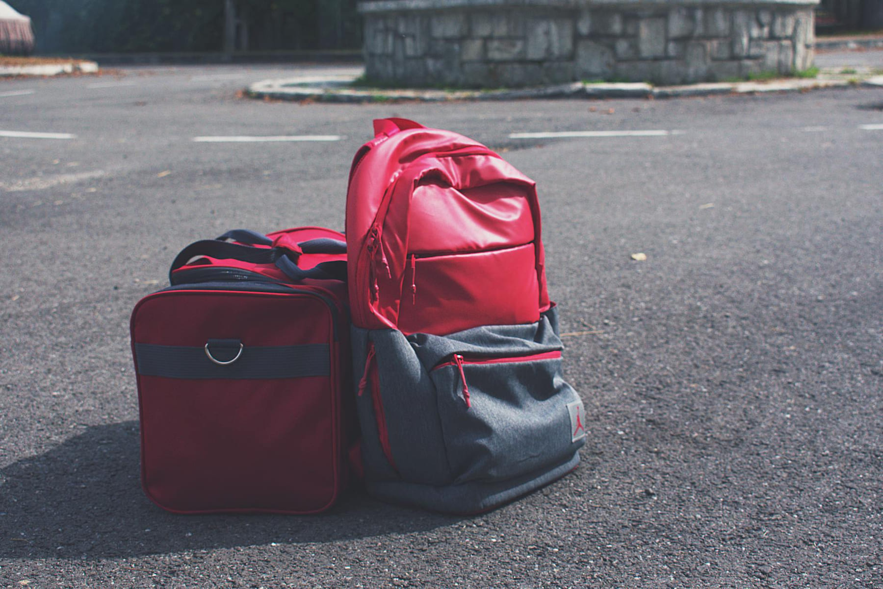 Red backpack and matching bag on asphalt, perfect for travel themes. on Miles and Memories