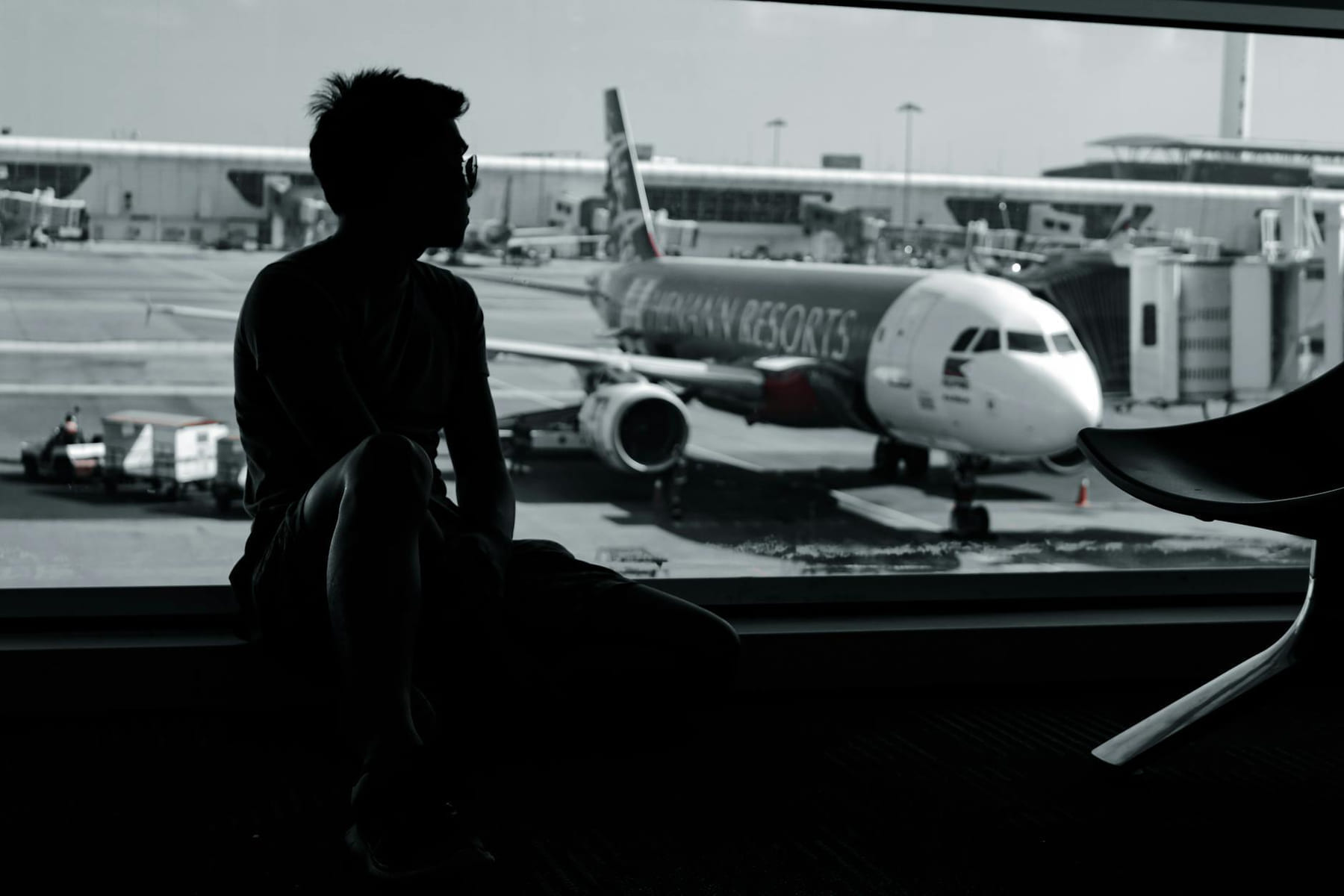 A silhouetted man sits in an airport terminal, viewing an airplane on the tarmac. on Miles and Memories
