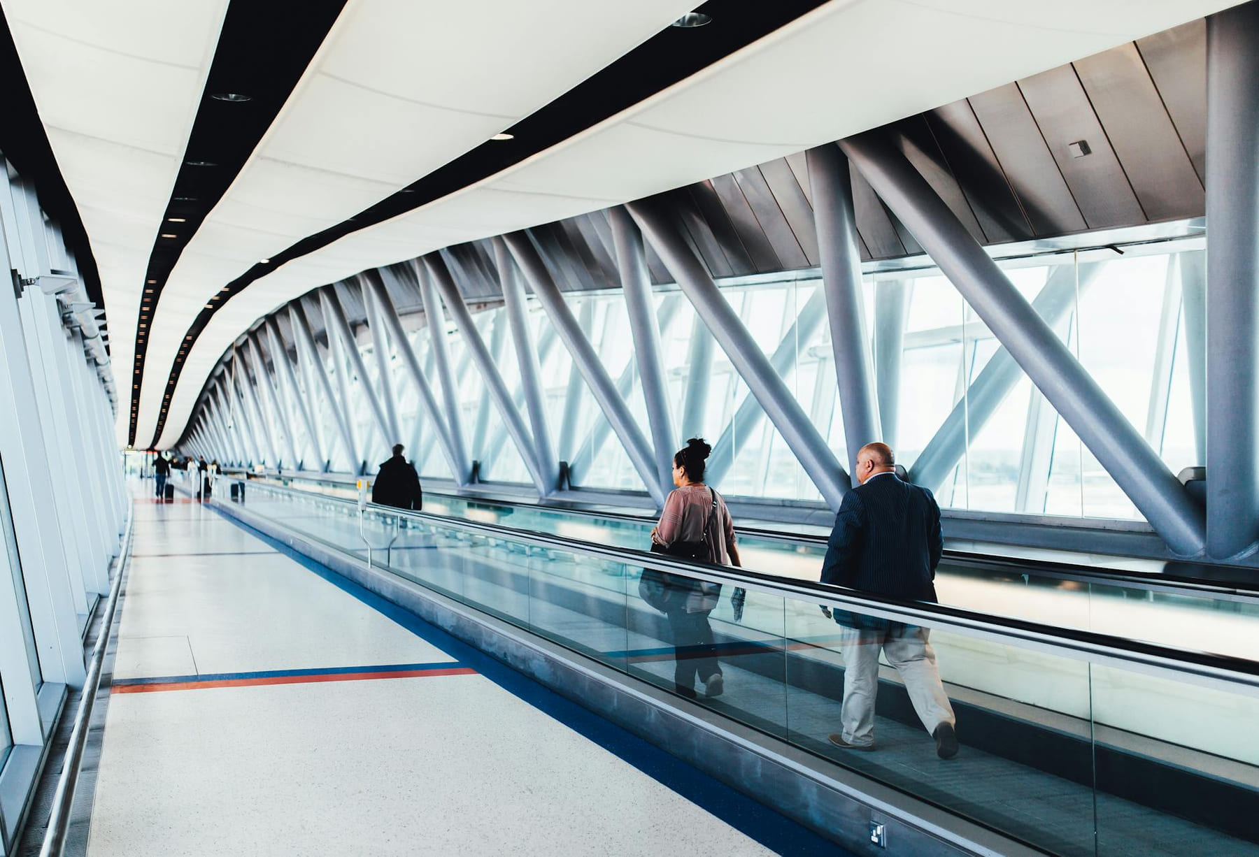 Travelers walking through a bright modern airport corridor with glass walls. on Miles and Memories