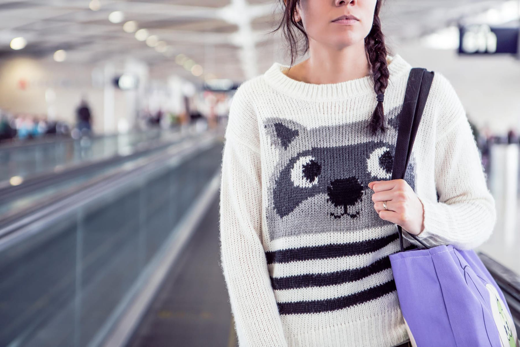Stylish woman in knit sweater with raccoon design carrying bag in airport. on Miles and Memories
