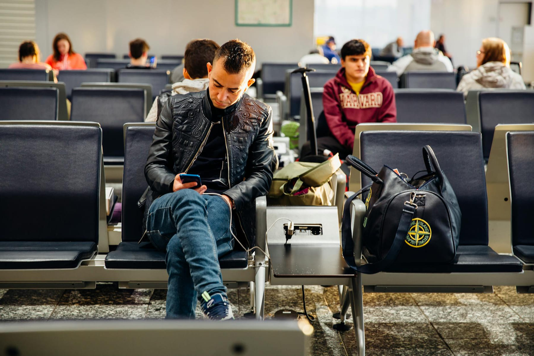 People sitting in an airport lounge, focused on smartphones and waiting for flights. on Miles and Memories