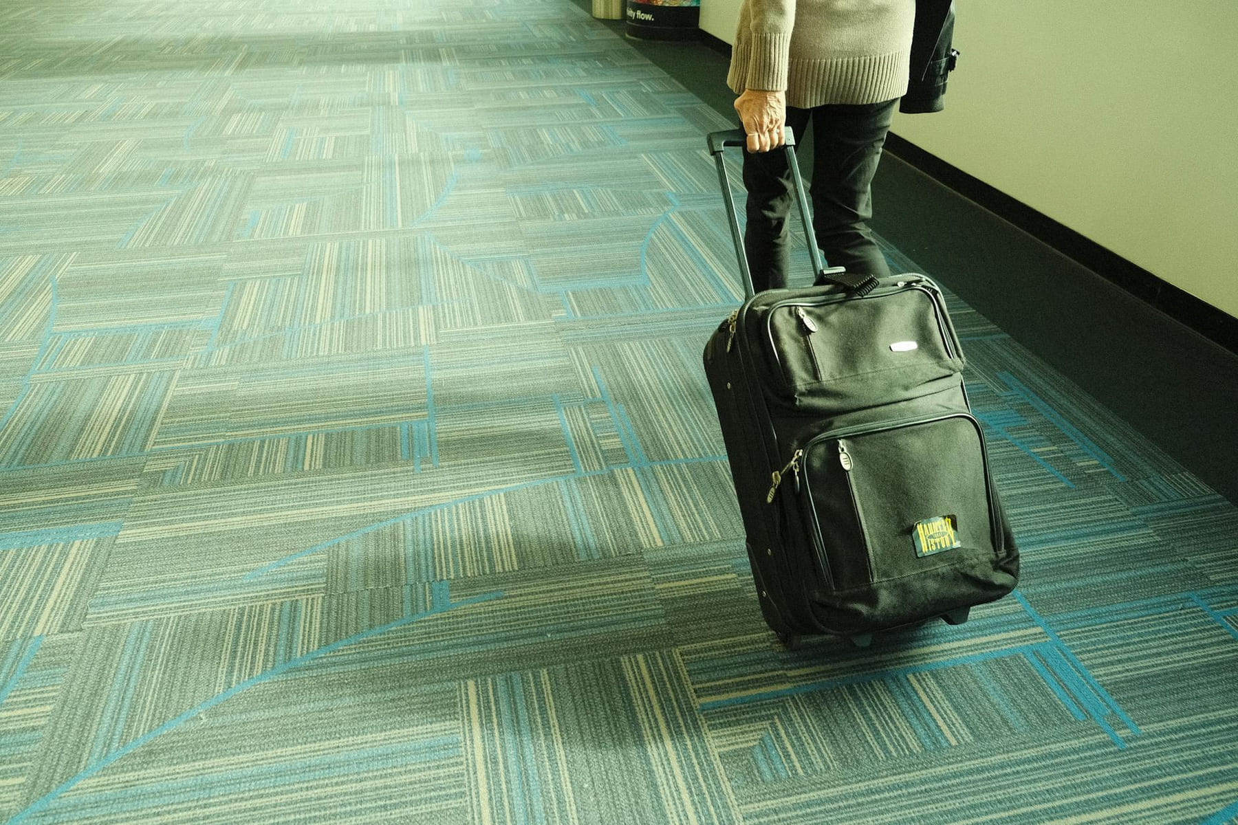 Person walking with luggage on blue carpeted airport corridor, traveling on Miles and Memories