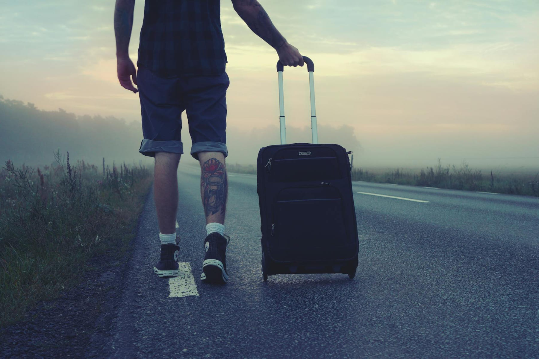 Man walking with a suitcase along a foggy road at sunrise, symbolizing adventure and travel. on Miles and Memories